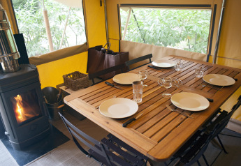 Mesa preparada para cuatro en tienda safari Trappeur con estufa de leña en Village Huttopia Lac de Rillé, Francia.