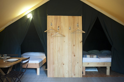 Interieur van de Trappeur safaritent in Village Huttopia Lac de Rillé, Frankrijk, met twee bedden en eetruimte.