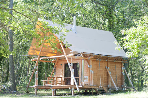 De Cahutte safaritent bij Village Huttopia Lac de Rillé, Frankrijk, omringd door groene bossen.