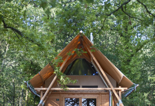 Tienda safari Cahutte en Village Huttopia Lac de Rillé, Francia, rodeada de árboles y personas descansando.