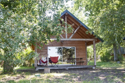 Cabin in the forest at Village Huttopia Lac de Rillé, France, with a porch, chairs, and picnic table outside.