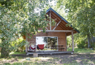 Cabaña de madera en el bosque de Village Huttopia Lac de Rillé en Francia, con terraza y sillas al frente.