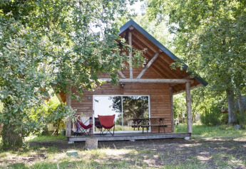 Cabane en bois dans la forêt au Village Huttopia Lac de Rillé, France, avec terrasse et deux chaises colorées.