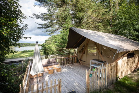 Safari tent with a wooden deck and lake view at Tente Trappeur Duo Village, surrounded by lush trees.