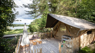 Safari tent with a wooden deck and lake view at Tente Trappeur Duo Village, surrounded by lush trees.