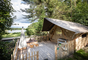 Safari tent met houten terras en zicht op het meer bij Tente Trappeur Duo Village, omgeven door groen.