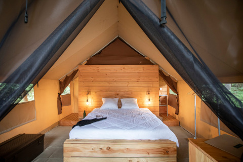Vista interior de una tienda safari con cama cómoda y detalles de madera en Huttopia Lac de Rillé, Francia.