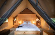 Vista interna di una tenda safari con letto comodo e dettagli in legno a Huttopia Lac de Rillé, Francia.