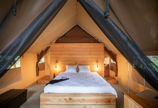 Vista interna di una tenda safari con letto comodo e dettagli in legno a Huttopia Lac de Rillé, Francia.