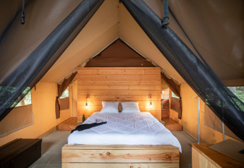 Vista interna di una tenda safari con letto comodo e dettagli in legno a Huttopia Lac de Rillé, Francia.