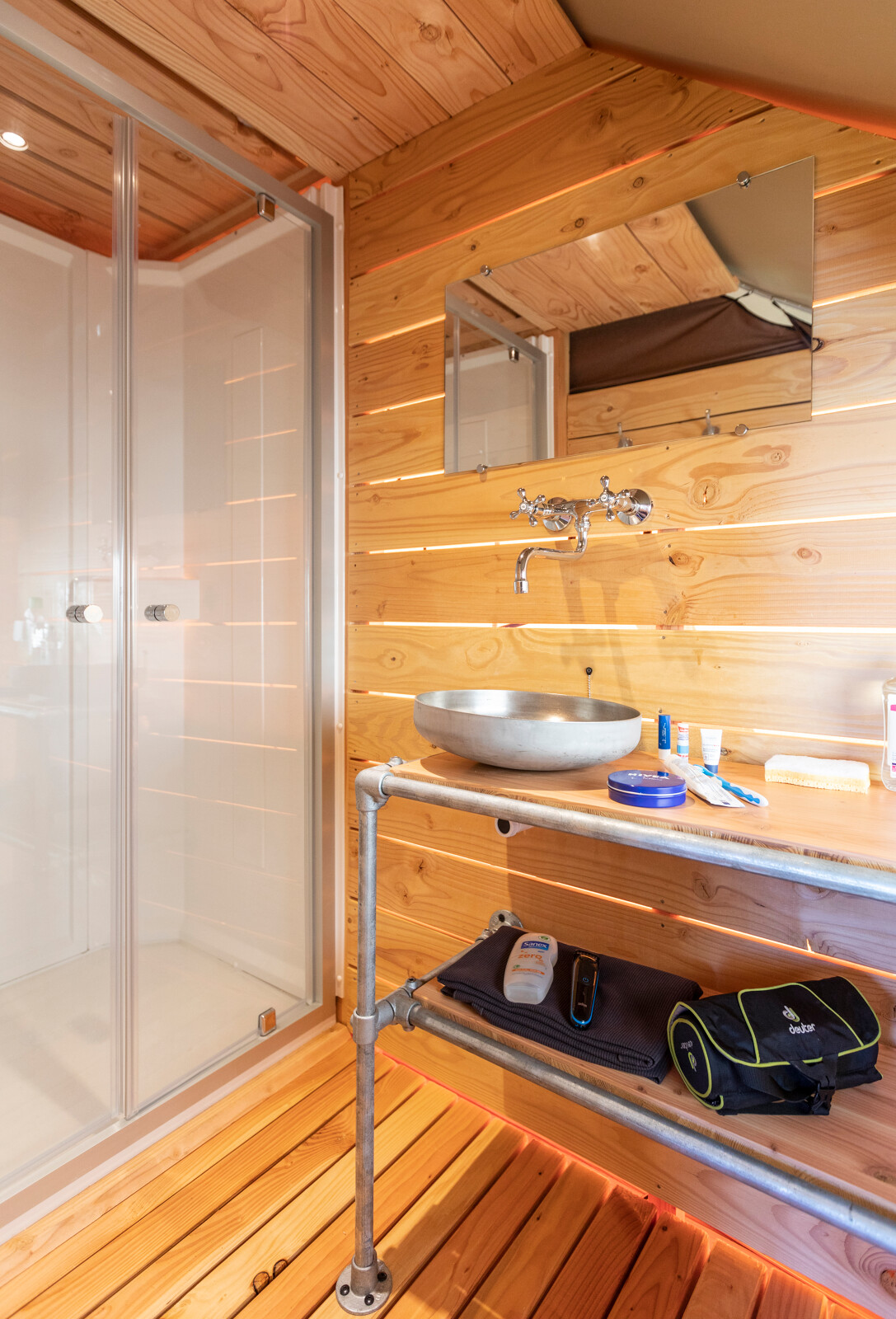 Badkamer met houten wanden, moderne wastafel en douche in een safaritent bij Huttopia Lac de Rillé.