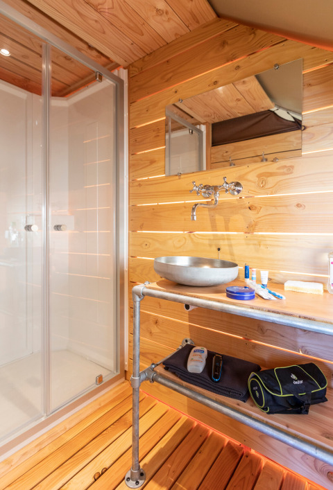 Baño con paredes de madera, lavabo moderno y ducha dentro de una tienda safari en Huttopia Lac de Rillé.