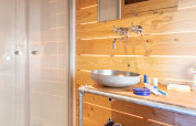 Baño con paredes de madera, lavabo moderno y ducha dentro de una tienda safari en Huttopia Lac de Rillé.