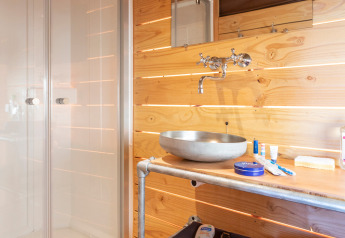 Baño con paredes de madera, lavabo moderno y ducha dentro de una tienda safari en Huttopia Lac de Rillé.