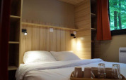Dormitorio del Chalet Evasion en Camping de Lyon con cama doble, bandeja con tazas y ventana al bosque.