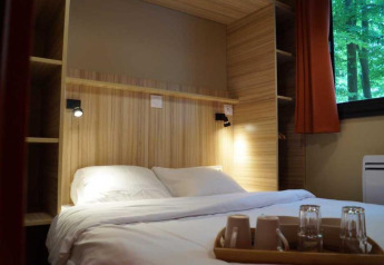 Schlafzimmer im Chalet Evasion im Camping de Lyon mit Doppelbett, Tablett und Blick ins Grüne.