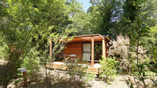 Cabaña de madera Chalet Evasion en un entorno natural verde, con terraza y sillas de jardín delante.