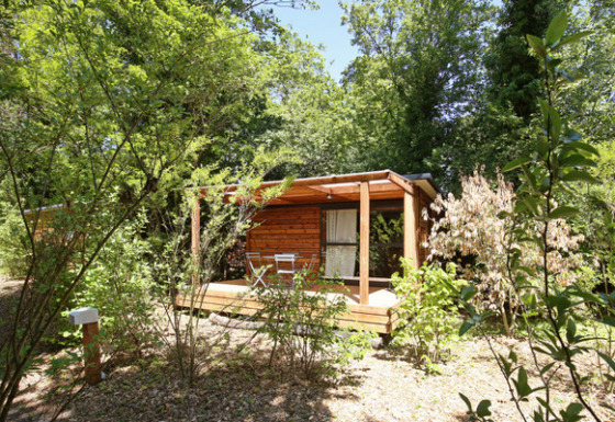 Træhytte kaldet Chalet Evasion omgivet af frodig, grøn natur, med terrasse og havemøbler foran.