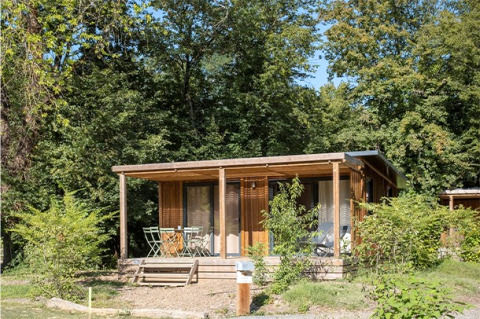 Außenansicht des Chalet Ottawa, einer gemütlichen Holzhütte mit Veranda, umgeben von viel Grün und Bäumen.