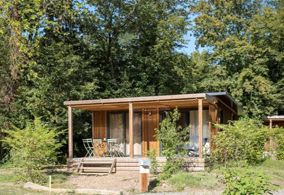 Außenansicht des Chalet Ottawa, einer gemütlichen Holzhütte mit Veranda, umgeben von viel Grün und Bäumen.