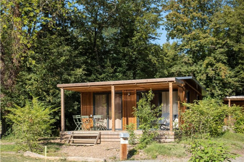 Vista exterior del Chalet Ottawa, una acogedora cabaña de madera con porche, rodeada de vegetación y árboles altos.