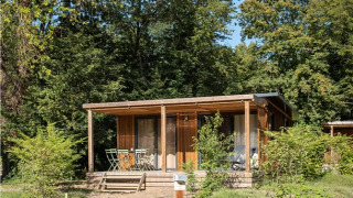 Vista exterior del Chalet Ottawa, una acogedora cabaña de madera con porche, rodeada de vegetación y árboles altos.