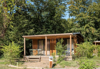 Vista esterna del Chalet Ottawa, una accogliente baita in legno con veranda, circondata da alberi e verde lussureggiante.