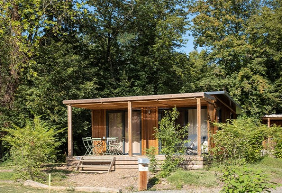 Vista exterior del Chalet Ottawa, una acogedora cabaña de madera con porche, rodeada de vegetación y árboles altos.