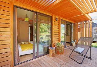 Holzveranda mit Loungestuhl, Pflanzen und Blick ins Schlafzimmer im Chalet Ottawa, Camping de Lyon, Frankreich.