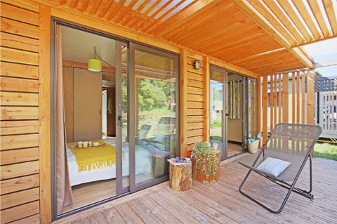 Terraza de madera con silla y vista al dormitorio en Chalet Ottawa, Camping de Lyon, Francia.