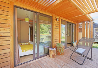 Terraza de madera con silla y vista al dormitorio en Chalet Ottawa, Camping de Lyon, Francia.