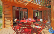 Terraza exterior en Chalet Ottawa, Camping de Lyon, Francia, con sillas y mesa rojas bajo pérgola de madera.
