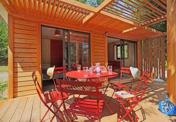 Terrazza esterna dello Chalet Ottawa, Camping de Lyon, Francia, con sedie rosse e tavolo sotto pergola in legno.