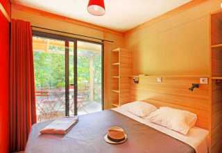 Helles Schlafzimmer im Chalet Ottawa, Camping de Lyon, Frankreich, mit Doppelbett und Terrassenzugang.