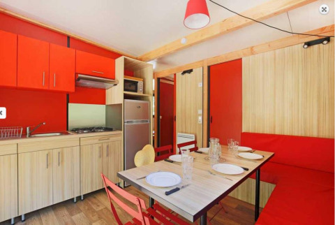 Cocina moderna y comedor en Chalet Ottawa, Camping de Lyon, con decoración roja y paneles de madera.