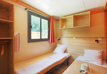 Due letti singoli in una camera luminosa allo Chalet Ottawa, Camping de Lyon, Francia, con finestra e scaffali.