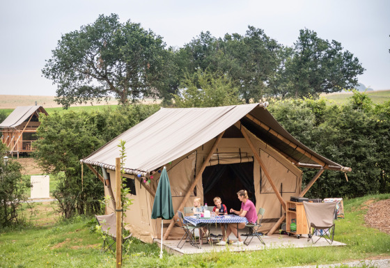 Una familia se sienta en una mesa frente a una tienda safari llamada Tent Trappeur, rodeada de naturaleza.