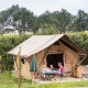 En familie sidder ved et bord foran en safari telt ved navn Tent Trappeur, omgivet af natur.