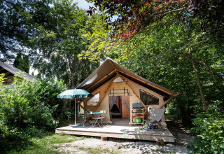 Tienda safari con terraza de madera y mobiliario exterior en Huttopia Pays de Cordes sur Ciel, rodeada de árboles.
