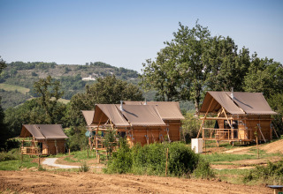 Vier Safari-Zelte namens Cahutte im Huttopia Pays de Cordes sur Ciel in Frankreich, umgeben von Natur.