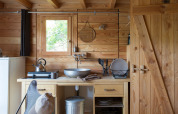 Acogedora cocina de una tienda safari Cahutte con paredes de madera, fregadero y utensilios.