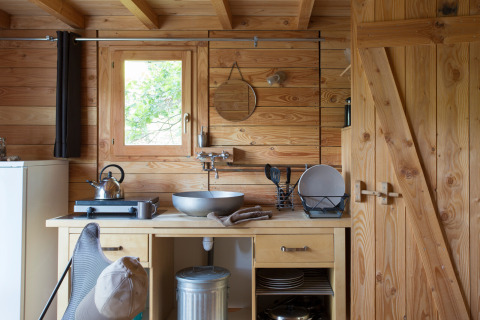Acogedora cocina de una tienda safari Cahutte con paredes de madera, fregadero y utensilios.