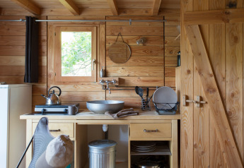 Acogedora cocina de una tienda safari Cahutte con paredes de madera, fregadero y utensilios.