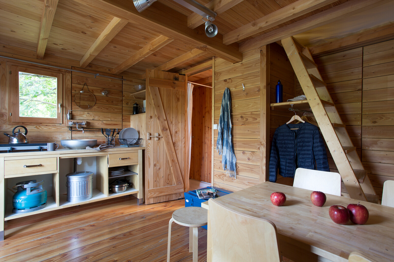 Interieur van een safaritent genaamd Cahutte met houten meubels, keuken en vier rode appels op tafel.