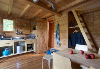 Innenraum eines Safari-Zelts namens Cahutte mit Holzmöbeln, Küche und vier roten Äpfeln auf dem Tisch.