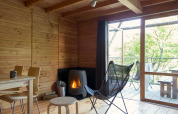 Innenraum des Safari-Zeltes Cahutte mit Holzverkleidung, Ofen und Ausblick auf eine grüne Terrasse.