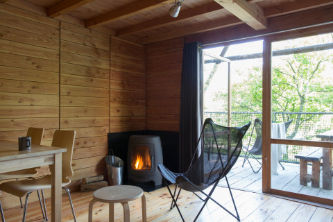 Interior de la tienda safari Cahutte con paredes de madera, estufa y terraza con vistas a la naturaleza.