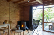 Interior de la tienda safari Cahutte con paredes de madera, estufa y terraza con vistas a la naturaleza.