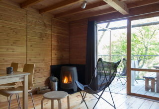 Interior de la tienda safari Cahutte con paredes de madera, estufa y terraza con vistas a la naturaleza.