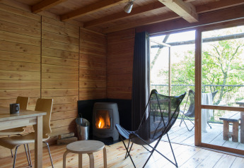 Interior de la tienda safari Cahutte con paredes de madera, estufa y terraza con vistas a la naturaleza.